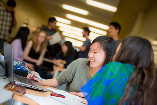 Students working together at a table with a laptop in a busy academic environment.